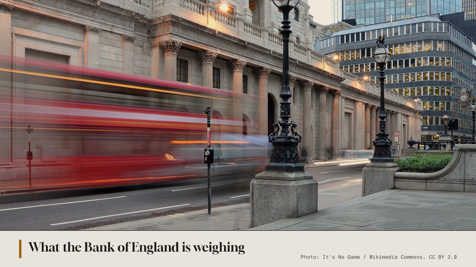 The Bank of England's columned facade at dusk on Threadneedle Street, a red bus blurred in motion past a black lamp post.
