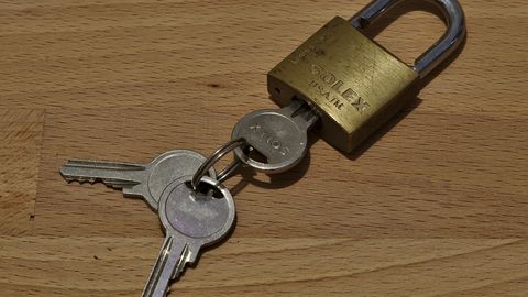 A brass padlock with two small keys on a wooden table