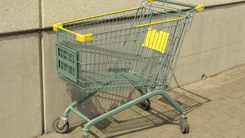 An empty green shopping trolley against a wall