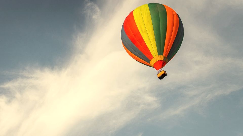 A striped hot air balloon rising into a blue sky