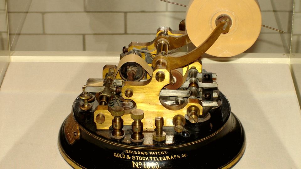 An antique brass stock ticker machine under a museum light